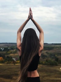 Rear view of woman with arms raised meditating against sky