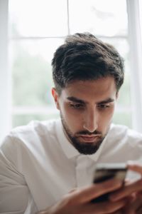 Man using mobile phone against window