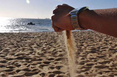 Cropped image of hand throwing sand at beach