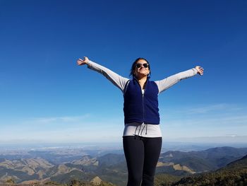 Young woman with arms raised standing on landscape against clear blue sky
