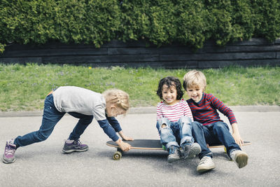 Girl pushing friends sitting on skateboard at yard