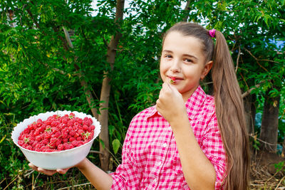 Portrait of smiling girl eating while holding raspberries in bowl