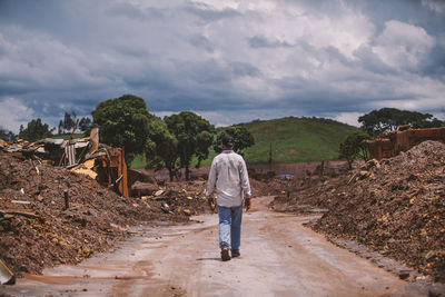 Rear view of man walking on road amidst damaged houses by tsunami