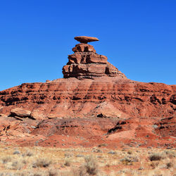 Rear view of man standing on rock formations in desert against clear sky