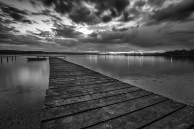 Pier over lake against cloudy sky