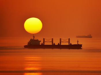 Silhouette boat in sea against orange sky