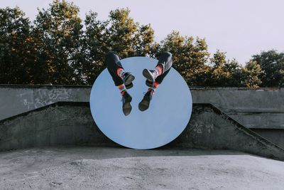 Low section of person sitting on mirror object at skateboard park