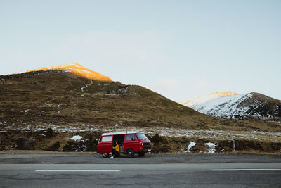 Young tourist in eyeglasses sitting in vintage automobile between deserted ground in snow near mountains