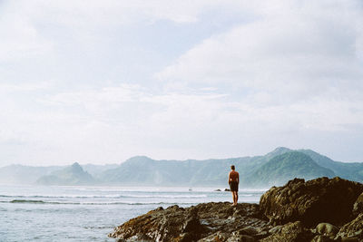 Rear view of woman standing on sea shore against sky