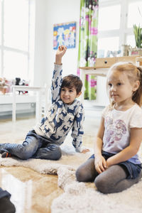 Happy boy raising hand while sitting by girl in classroom