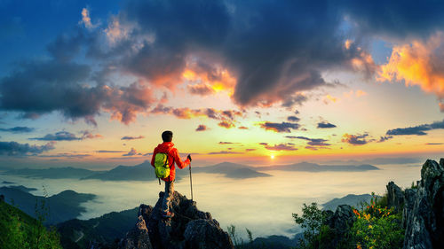 Rear view of man standing on mountain against sky during sunset