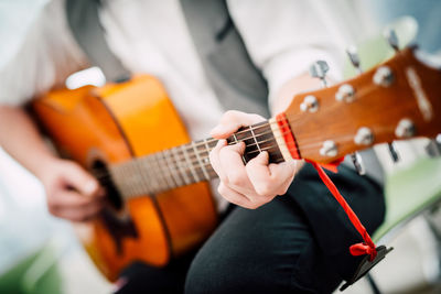 Midsection of male guitarist playing acoustic guitar while sitting on chair