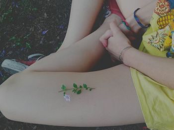 Flower on thigh of young woman sitting on field