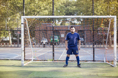 Portrait of serious soccer player standing against goal post at field