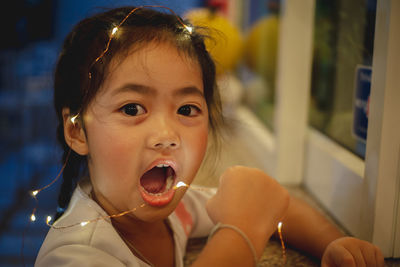 Close-up portrait of cute girl with mouth open holding illuminated lights