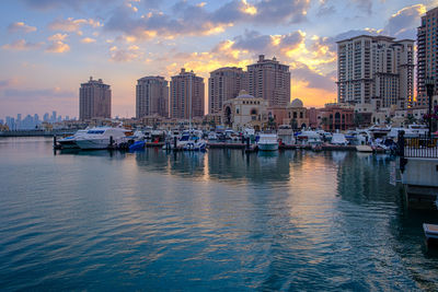 Boats moored in sea against buildings in city during sunset