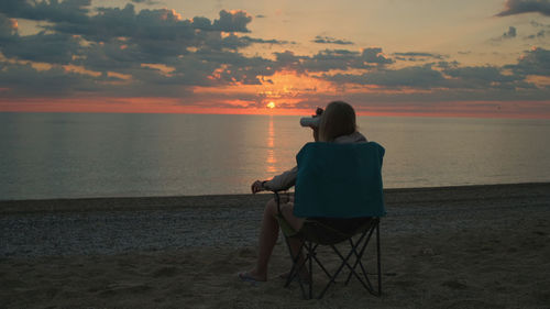 Rear view of woman sitting on beach during sunset