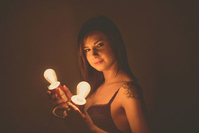 Portrait of sensuous young woman holding illuminated lights in darkroom