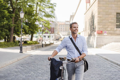 Smiling man pushing bicycle in the city