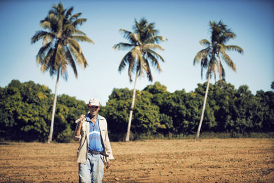 Man carrying hand tool while walking on field against blue sky