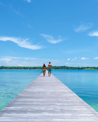 Rear view of woman walking on pier over lake against sky