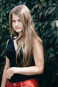 Portrait of beautiful young woman standing against plants