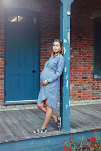Full length of pregnant woman standing against house