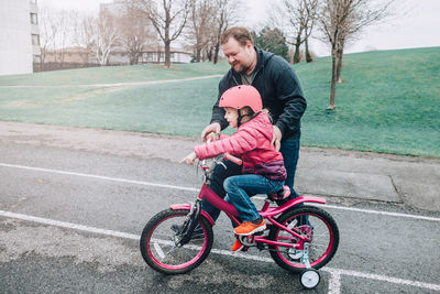 Man assisting daughter in riding bicycle on walkway