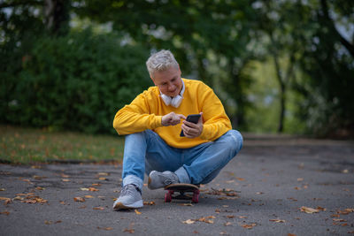 A woman sits on a skateboard and looks into her phone and does salfy