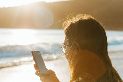 Young woman using mobile phone while standing on beach