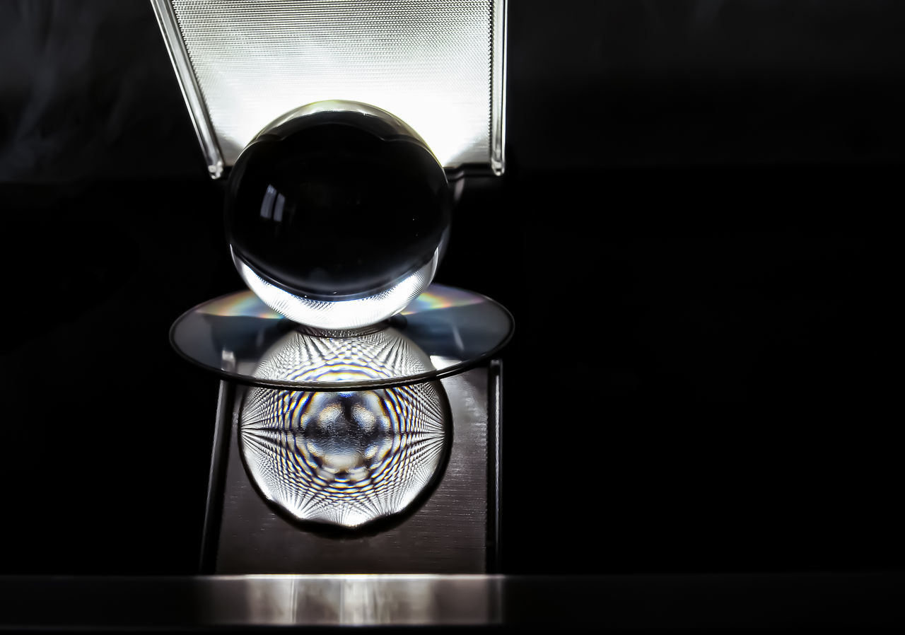 close-up, reflection, no people, glass - material, indoors, still life, table, transparent, crystal ball, focus on foreground, sphere, technology, copy space, shape, black background, single object, glass, dark, nature