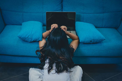 Rear view of woman using mobile phone while sitting on sofa