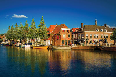 Boats in river by buildings against sky