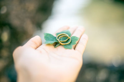 Close-up of cropped woman hand holding wedding rings with leaf