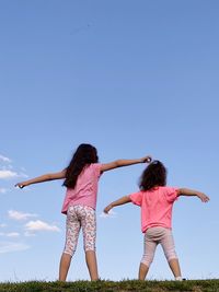 Rear view of two girls with arms outstretched against sky