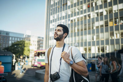 Male tourist looking away while standing against building