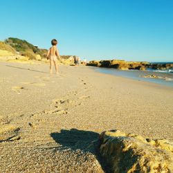 Rear view of man walking on beach against clear sky