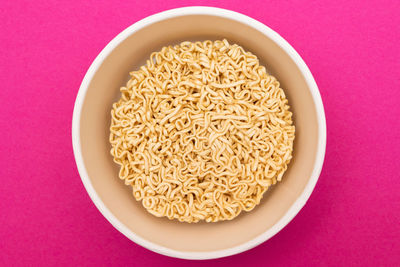 Opened package with uncooked instant noodles on pink background