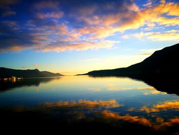 Scenic view of river and silhouette mountains against cloudy sky during sunset