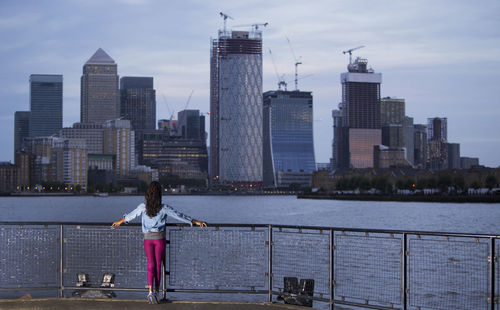 Rear view of woman standing by river with buildings in background