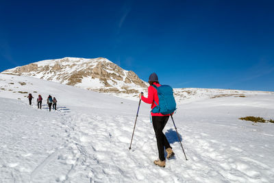 A woman walking on the snow in the mountains, towards the summit, on a sunny winter day.