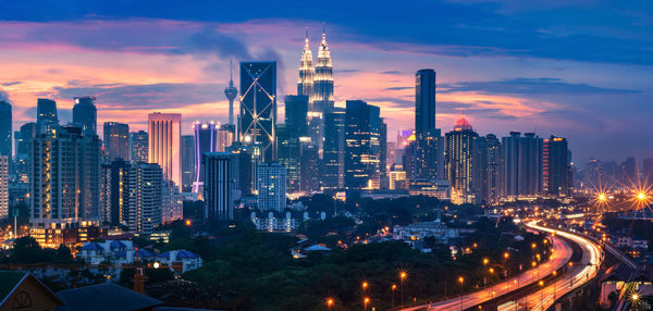 Illuminated buildings in city against sky during sunset