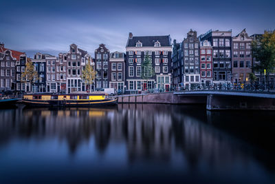 Bridge over river by buildings in city against sky at dusk