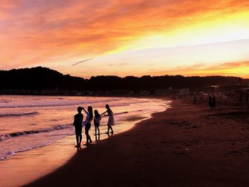 Silhouette people on beach against sky during sunset