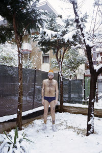 Portrait of shirtless young man standing on snow covered field