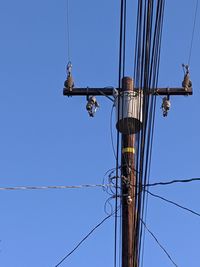 Low angle view of electricity pylon against clear blue sky