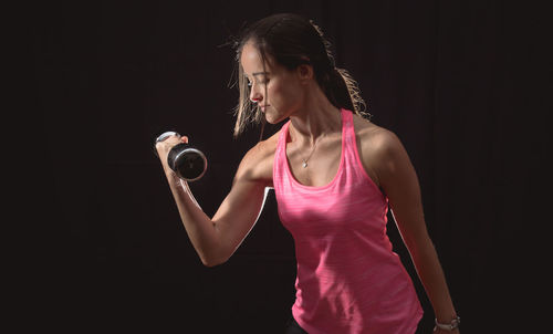 Mid adult woman exercising against black background