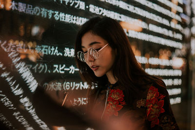 Close-up of young woman using mobile phone standing outdoors at night