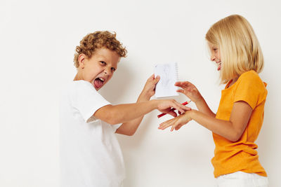 Side view of sibling holding book standing against white background