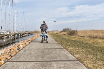 Grandfather riding granddaughter in baby carriage on footpath